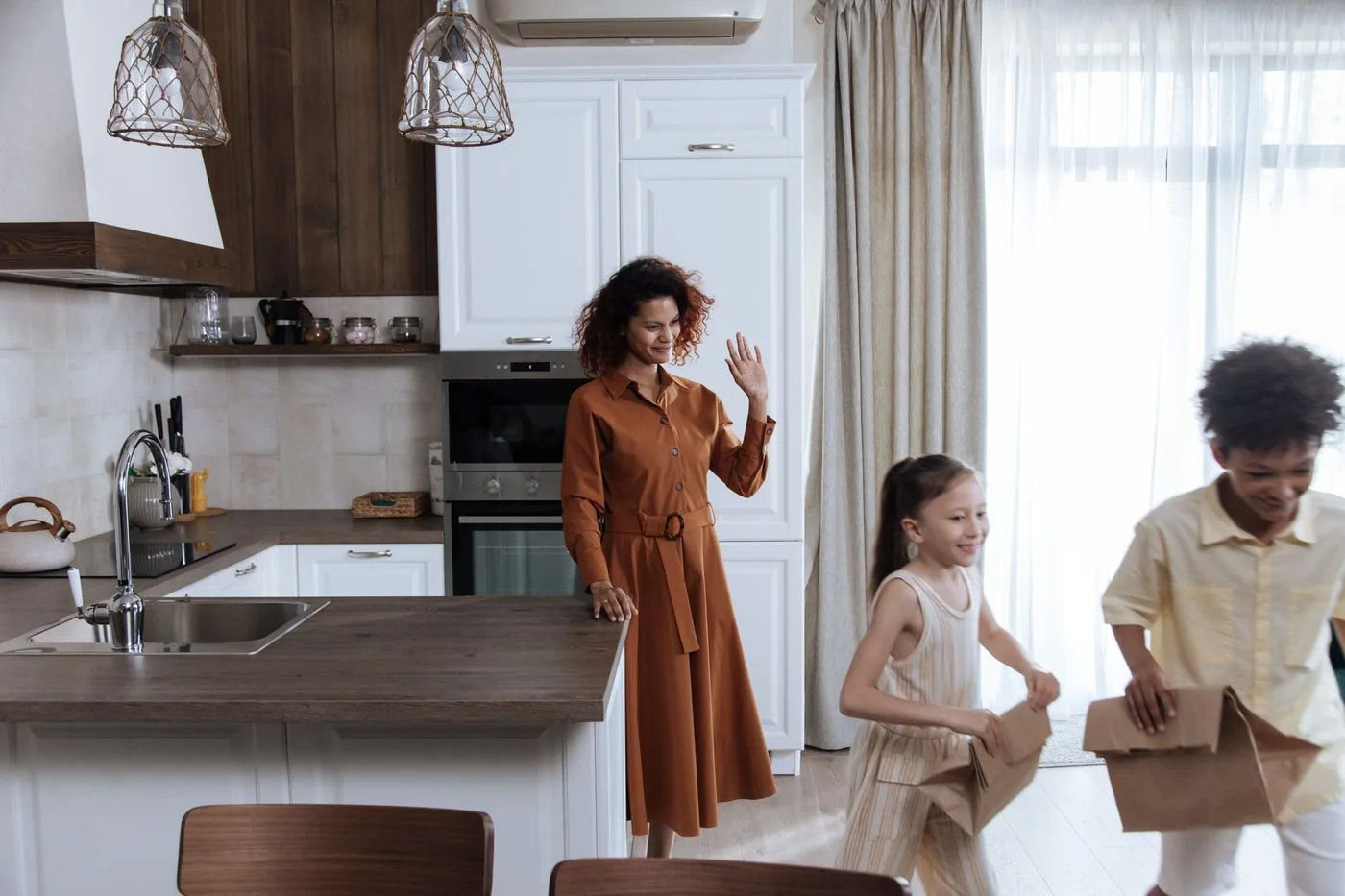 Children carrying lunch bags beside their mother in a kitchen